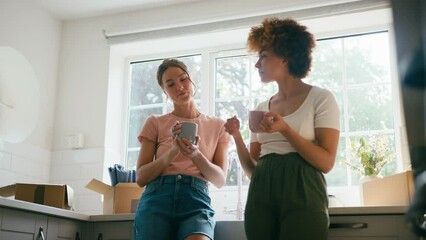 Two female friends or same sex couple taking a coffee break from unpacking in kitchen on moving day in new home - shot in slow motion - Powered by Adobe