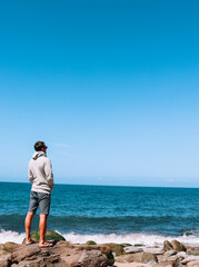 Young man traveler contemplating in a peaceful place in fornt of the ocean viewed from the back....