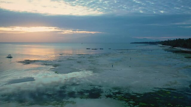 Filipino teenagers watching sunset on Tubod beach, Siquijor island, Philippines. Fisherman in the sea. Cinematic aerial drone view at sunset. Vibrant cloudy sky colors. Famous travel destination.
