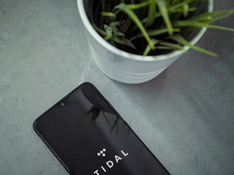 Lod, Israel - July 16,2023: Modern workspace with smartphone with TIDAL Music app launch screen on marble background. Close up top view flat lay.