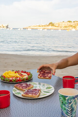Fototapeta na wymiar Woman's hand taking a toast from a breakfast served at the beach with the sea in the background