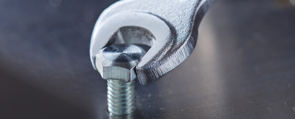 Wrench tightens bolt in steel billet. Spanner, bolt, screw and nuts.