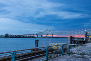 Obraz premium a gorgeous summer landscape along the Mississippi River with the Crescent City Connection bridge over the water with blue sky and powerful clouds at sunset in New Orleans Louisiana USA
