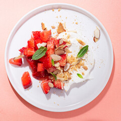 Strawberry Whipped Cream Recipe or Strawberry Fool served with mint, almond flakes and cookies  on a white dish, pink background. Minimalist light recipe of dessert. Square crop