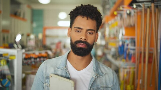Portrait of small business owner. Confident Bearded black man with tablet walking shop aisle in hardware store