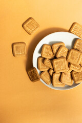 Butter cookies stacked on white plate on yellow background. Copy space.