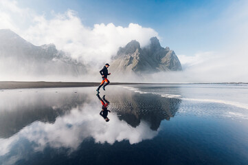 A runner in distance is running in nature on the ocean shore. There are mountains in the background.