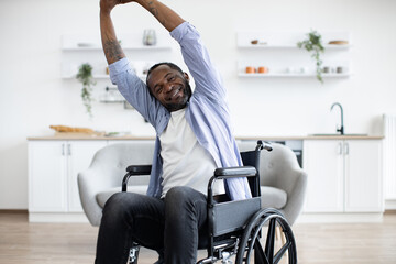 Close up of delighted african male working out while raising hands staying in good mood on sunny day at home. Smiling mature person increasing endurance while doing exercise with disability.