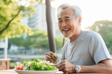 Asian old man eating healthy salad after exercising in the park in sportswear during the day