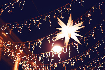 Christmas background. Decorative luminous star, bright festive street lighting with light bulbs and garlands. New Year's decor on the city streets.