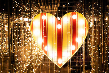 Christmas background. Valentine's day background. Decorative heart illuminated with bright light bulbs and garlands. New Year's decor on the city streets.