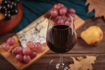 Glass of red wine served with blue cheese on dark wooden background. Autumn picnic with wine and cheese platter, fruits and dry leaves in rustic style