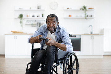 Close up view of african male gamer with mobility impairment with input devices in spacious kitchen...