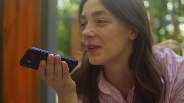 Young woman recording voice message sitting on swing in the park close-up. Chatting with friends outdoors