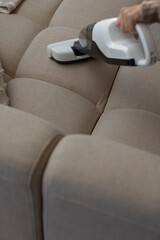 Wireless handheld vacuumer cleaning beige neutral color couch.