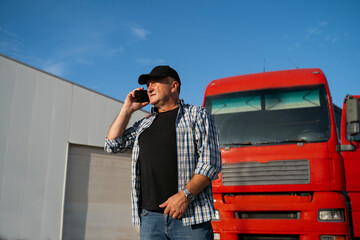 Trucker talking on phone and standing in front of his truck 