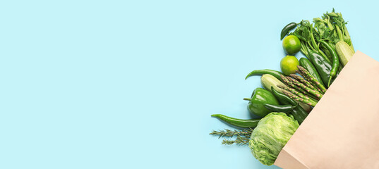 Paper bag with different green vegetables on light blue background with space for text