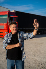 Positive middle age trucker
waving to collogues, standing in front of vehicle , vertical shot