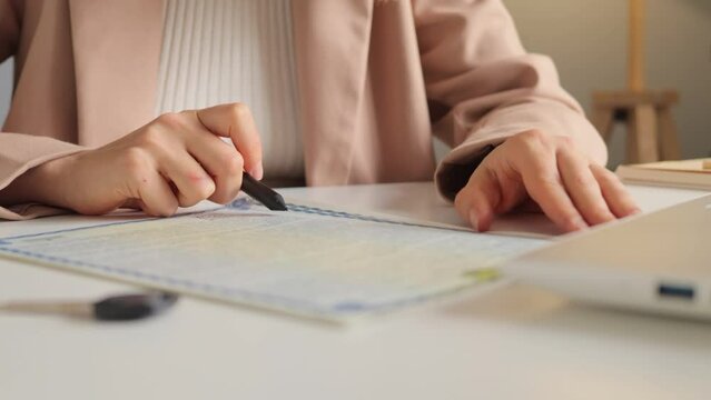 Unknown woman preparing documents to assist people in relocating to new house sitting at her workplace in real estate agency signing papers.
