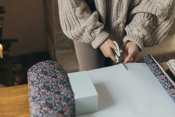 Wrapping christmas gifts. Hands in cozy sweater cutting stylish festive wrapping paper with...
