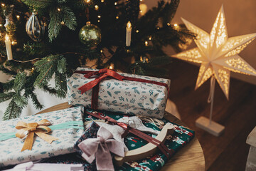 Stylish christmas gifts in festive wrapping paper with bows, vintage ornaments, toy on wooden table...