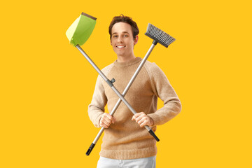 Young man with broom and dustpan on yellow background - obrazy, fototapety, plakaty