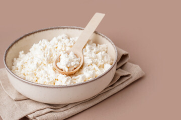 Bowl with tasty cottage cheese on beige background