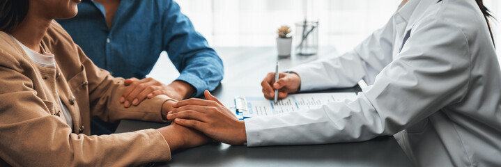 Doctor providing compassionate healthcare consultation while young couple patient holding hand, comfort each other after infertile report. Reproductive and medical fertility consulting. Neoteric - obrazy, fototapety, plakaty