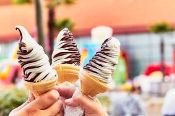 Three hands holding ice cream. Chocolate vanilla ice cream in waffle cups