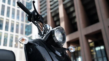 Black scooter stands in a financial district with skyscrapers. Close-up