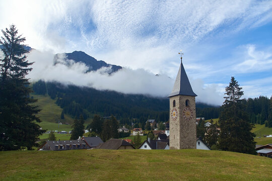 Beautiful swiss alpine countryside with a medieval bell tower with a clock and Rothorn mountain on background in Churwalden village in Switzerland formerly Parpan