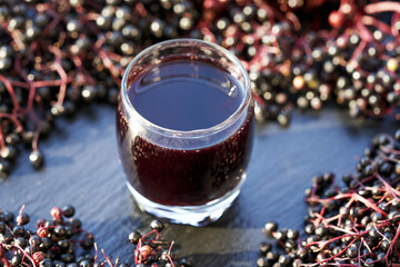Black elderberry syrup in a glass cup with fresh berries