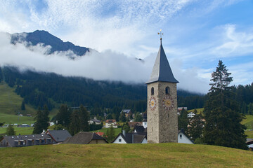 Beautiful swiss alpine countryside with a medieval bell tower with a clock and Rothorn mountain on background in Churwalden village in Switzerland formerly Parpan