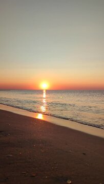 Beautiful sunrise on sea coast seaside. Sun rising from clouds in sky on blue sea with sea waves rolling on sandy beach. Bright shining sun. Seascape sea landscape. Natural nature background Vertical