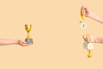 Female hands with gold cup and medals on beige background