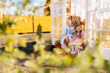 Remote view of cheerful blonde young mother in dress sitting on doorstep of summer gazebo house...