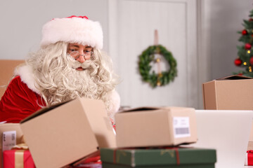 Santa Claus checking parcels at table in living room with Christmas decor