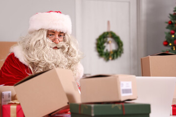 Fototapeta premium Santa claus working on laptop with christmas presents and shipping boxes, holiday season logistics and e-commerce, modern aspects of gift delivery and online retail during the festive period