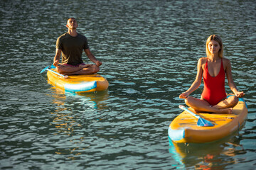 Man and woman practicing yoga on sup board, family outdoor summer sport activity.
