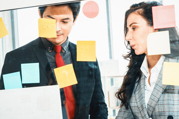 Business people work on project planning board in office and having conversation with coworker...
