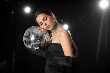 Stylish young woman with disco ball on dark background