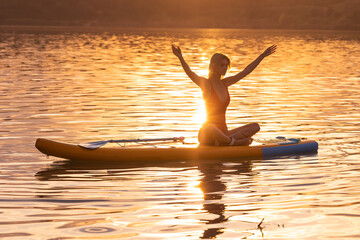 Beautiful woman practicing yoga on paddle sup surfboard.