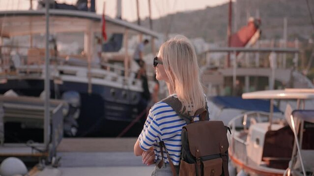 Female tourist with backpack at sunset walking and enjoying relaxing sea pier against background sailing ships and yachts, traveling in turkey summer vacation vacation, tourism beautiful destinations.