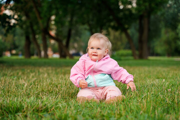 Cute caucasian kid baby sitting on the grass in a jacket
