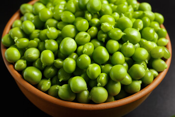 Perfect grains of fresh green peas in a ceramic bowl on a black background.