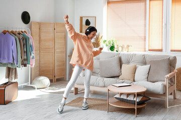 Young Asian woman in stylish hoodie with headphones dancing at home