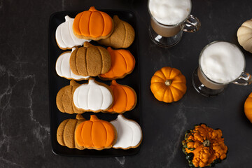 A plate of pumpkin-shaped cookies and a cup of latte on a dark background