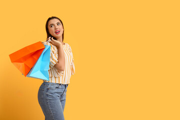 Beautiful young happy woman with shopping bags on yellow background