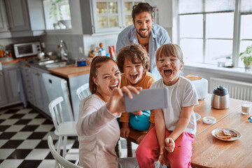 Happy young family taking a selfie in the kitchen after a messy breakfast