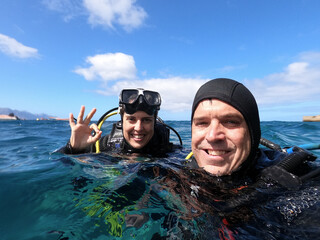 Couple, man and woman, of divers at sea surface smiling making the sign 